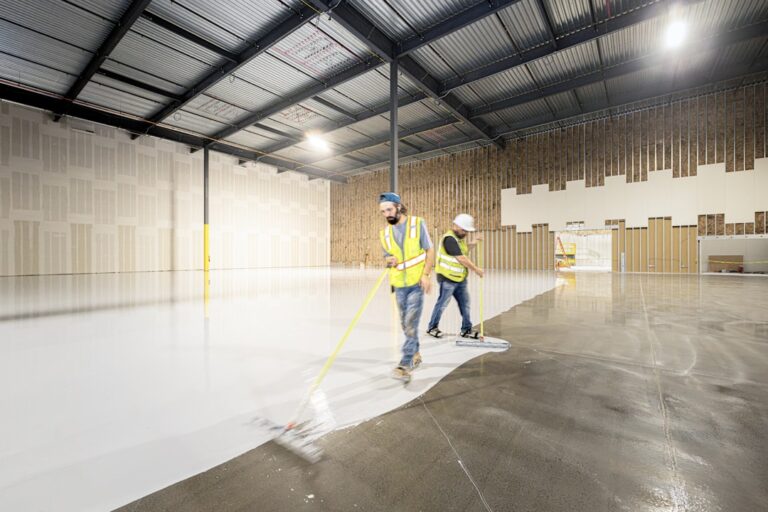 A person inspecting and gently cleaning a large coated warehouse floor with a mop and soft cloth.