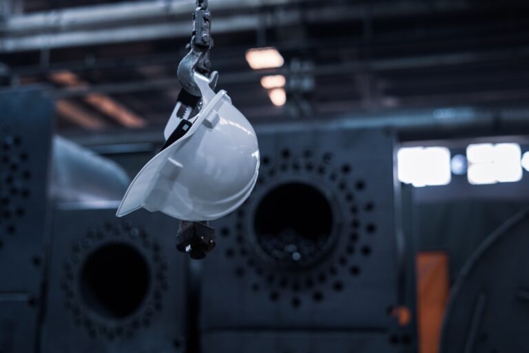 A technician inspects a metal railing while applying a protective industrial coating with spray equipment.