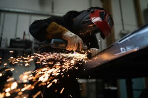 Workers apply protective coating to metal equipment inside a ventilated industrial workshop.